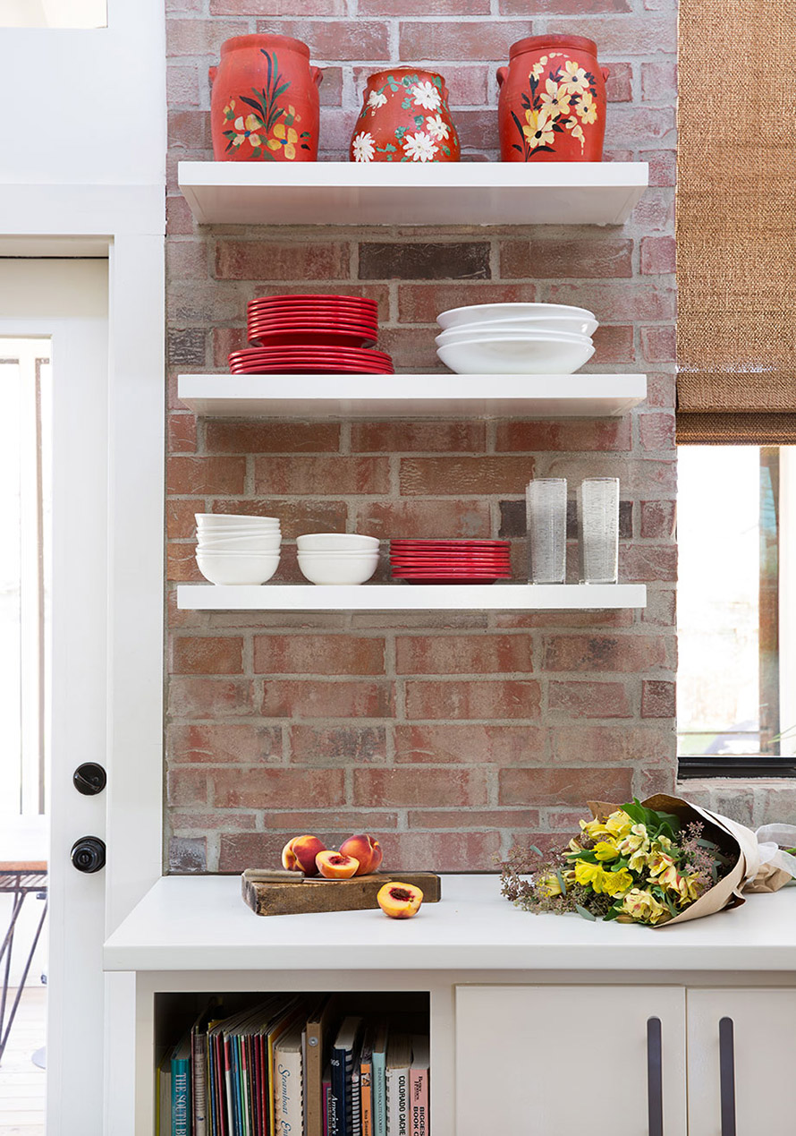 Colorful modern eclectic kitchen design. White open shelving with red and white dishes stacked neatly and a bouquet of flowers and peaches on the white countertop.