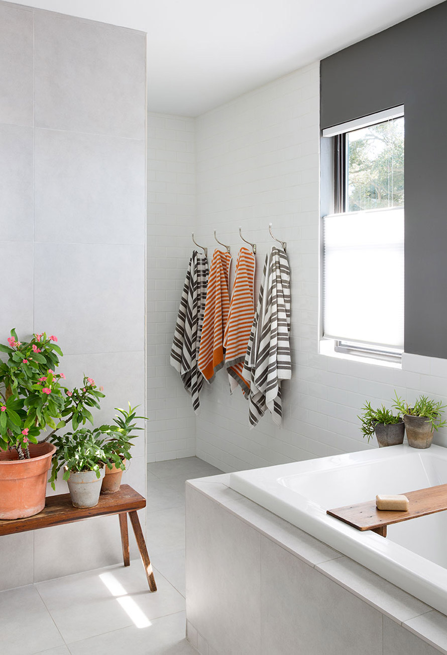 Minimalist white bathroom with four towels hanging and plants positioned around the tub.
