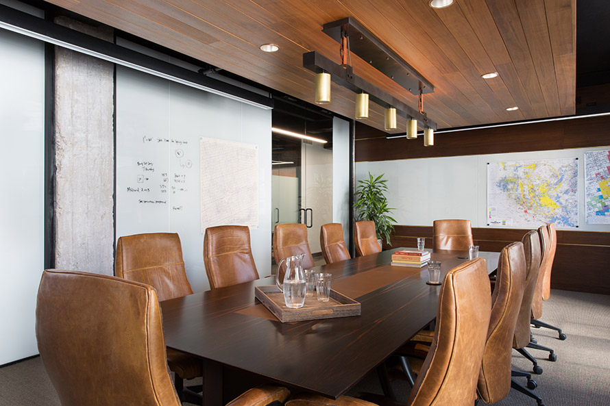 Invest firm board room with a long dark wood table and brown leather chairs.