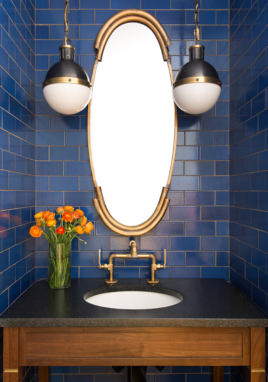 Bathroom sink with oval mirror and dark blue tile walls.