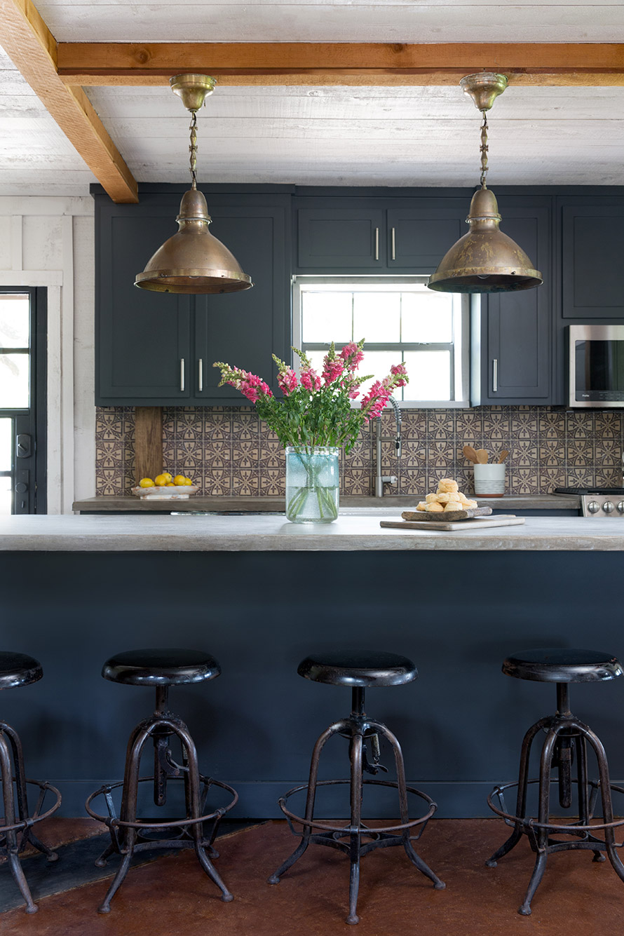 Kitchen with blue shelves, gold hanging light fixtures and antique black metal stools.