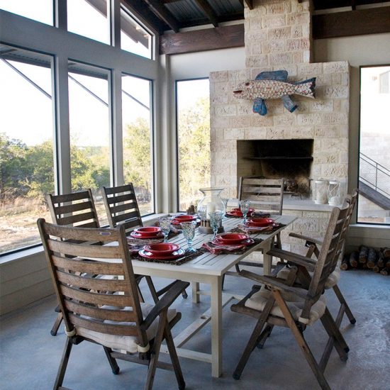Our portfolio includes a hill country retreat house with an indoor patio with a wood table and 6 chairs and a fireplace.
