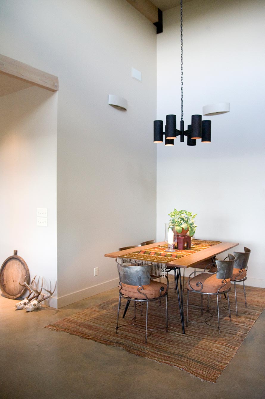 Concrete floor, high ceilings, black hanging light fixture, small dining room table.