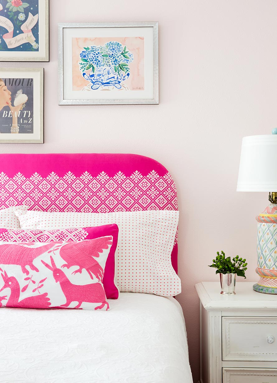 Close up of a bed with a hot pink and white headboard and cute framed photos on the wall.