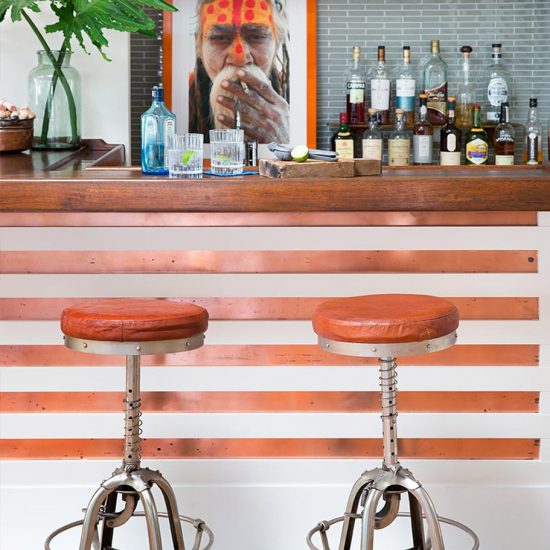 Our portfolio includes a house with a fully stocked bar with orange stripes and unique silver stools with orange cushions and a grey tile backsplash.