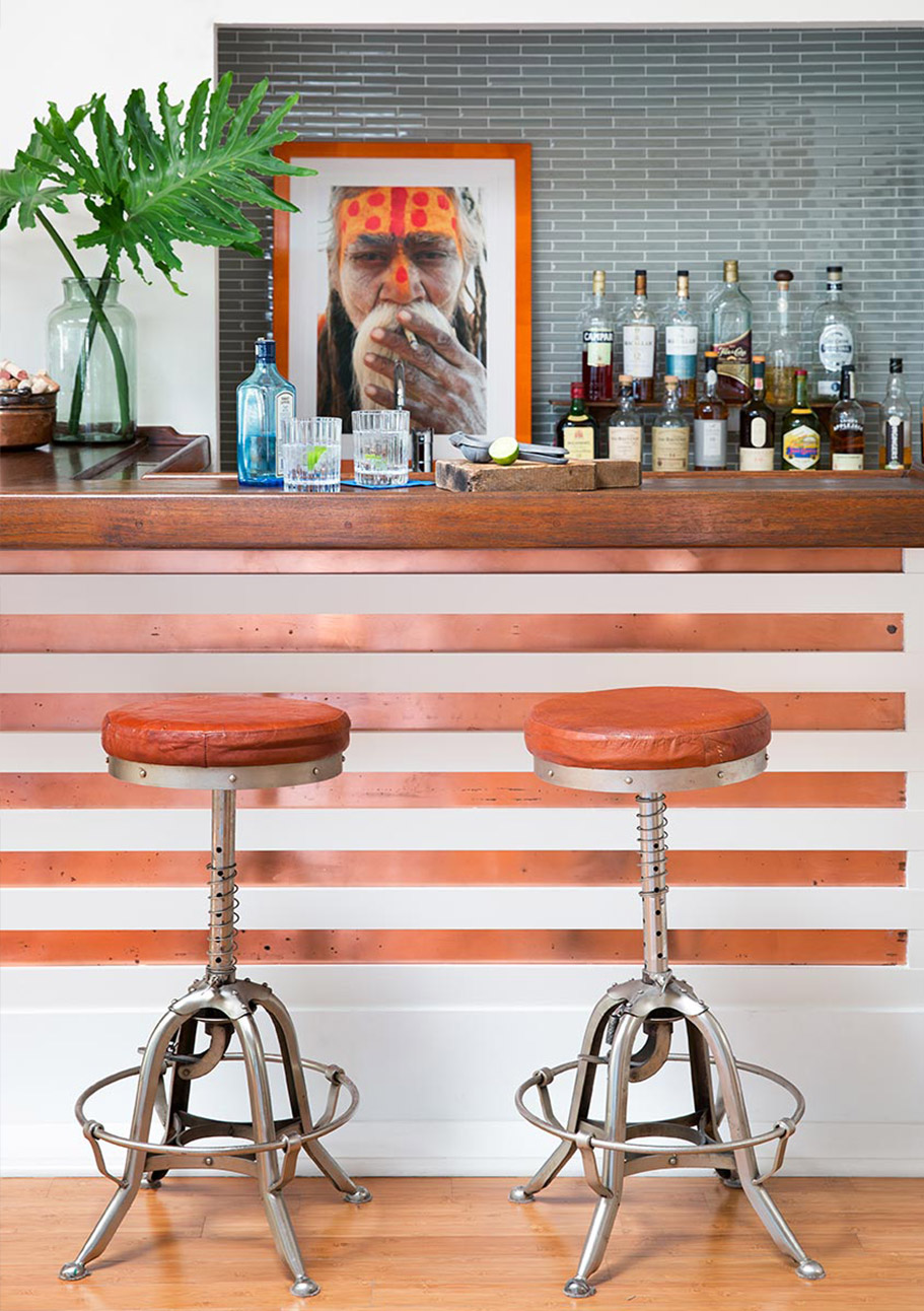 Our portfolio includes a house with a fully stocked bar with orange stripes and unique silver stools with orange cushions and a grey tile backsplash.