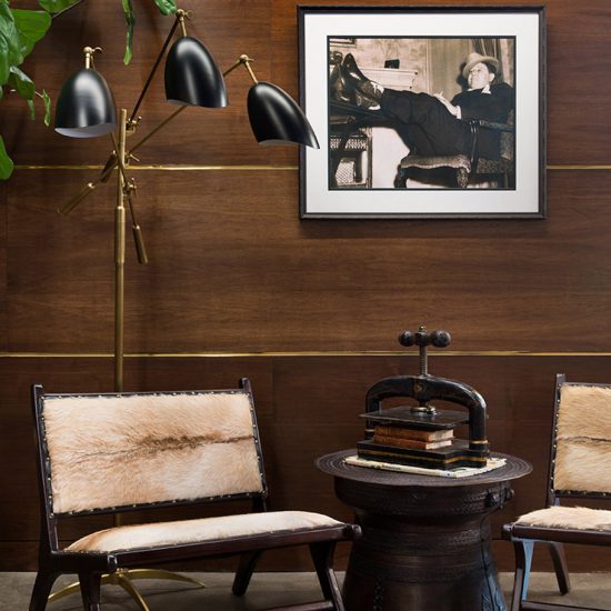 Our portfolio includes an investment firm headquarters with black and gold standing lamp, black and white photograph on the wall, dark wood walls with gold accents, a fiddle leaf fig, and two cute chairs with fur.