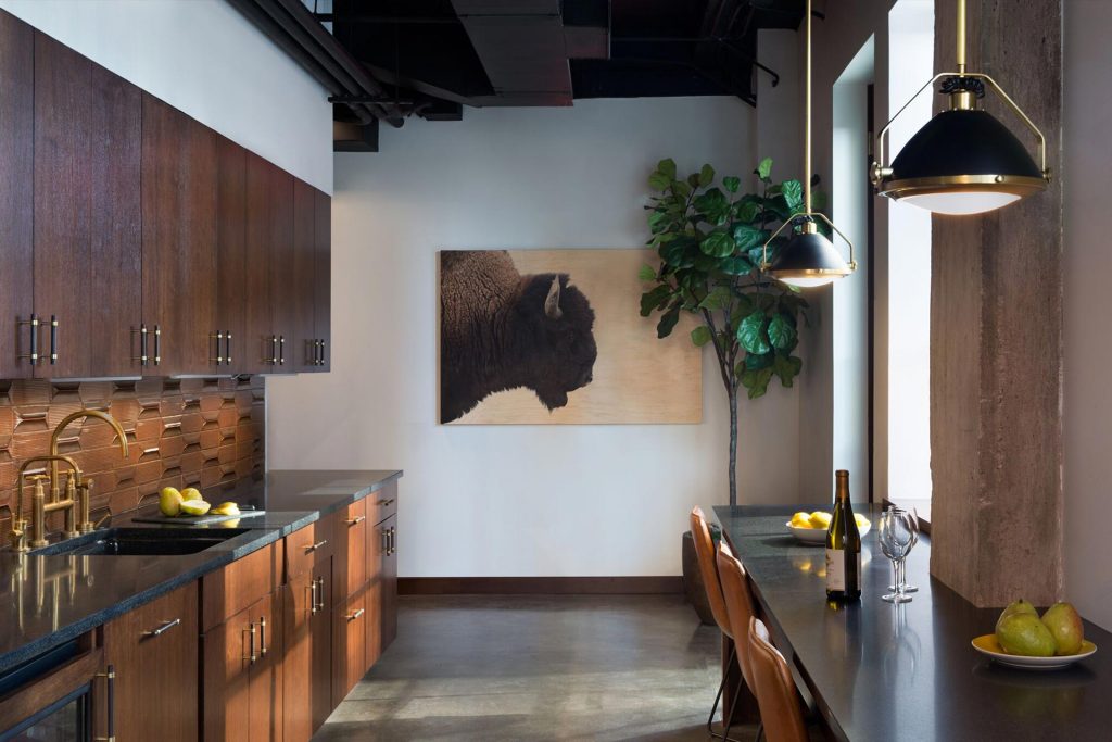 Investment firm kitchen with dark wood cabinets, beautiful brown tile backsplash, fiddle lead fig, black countertops, and buffalo painting.